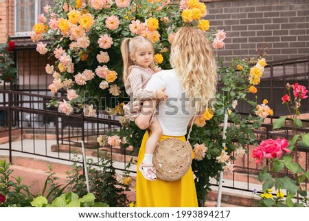 Mom and daughter admire the bushes of yellow roses, take selfies, take pictures. Spring landscape.