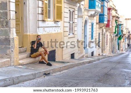 male tourist with retro camera taking pictures of maltese typical colorful balcony