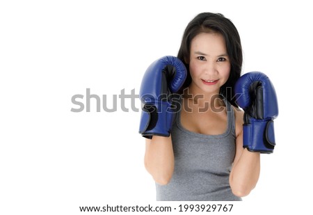 Determined young fit Asian female in blue boxing gloves standing in fighting stance and looking at camera with smile against white background