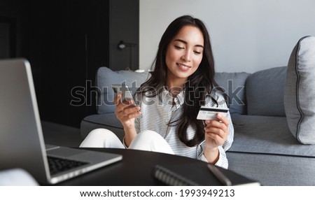 Portrait of young woman, asian girl shopping online, paying bills with credit card, laptop and smartphone, enter card number in mobile phone app to purchase smth in internet store Royalty-Free Stock Photo #1993949213