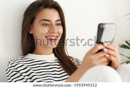 Close up portrait of smiling beautiful woman using smartphone, sitting comfortable with mobile phone, chat or watch videos on cellphone, texting message