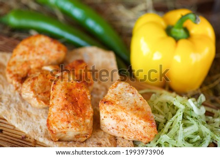 Pieces of grilled meat on pita bread, served with fresh peppers and salad on a wooden board and hay.

