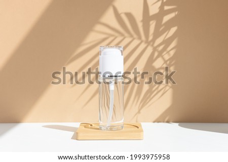 Reusable glass white bottle for oil, cream, lotion or serum on a beige background with a shadow of tropical palm leaves. Presentation of a cosmetic product. Layout of the beauty salon branding