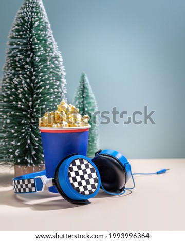 New Year holliday composition with disposable cup with popcorn, headphones and decorative christmas trees. Concept of playing games and watching movies on Christmas holidays, New Year holidays at home