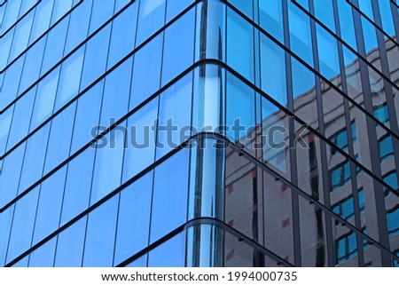 The corner of a modern glass building in Sydney central business district. Reflections of the sky and other buildings are in the glass facade