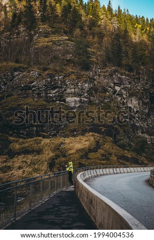 Girl in Yellow jacket taking a picture of  Mountain Range in Norway at the highway in autumn