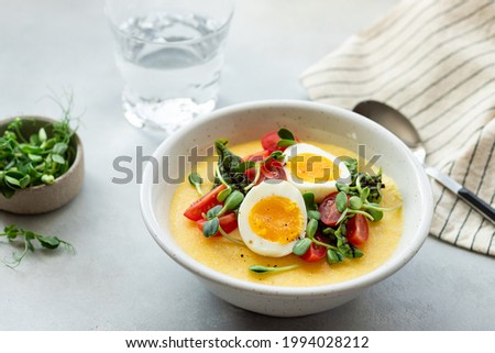 polenta bowl with fresh vegetables, microgreens and eggs on gray table. Healthy food concept. blurred background