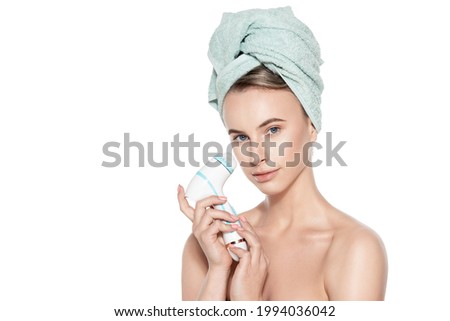 Young woman using sonic facial cleansing brush. Skincare and beauty concept portrait over white. Exfoliation, face massage, make up removal background.