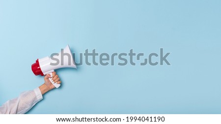 Business Hand holds a megaphone from a hole in the wall on blue background.  hiring, advertising, advertise and Banner concept.