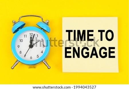 Business and finance concept. On a yellow background lie a clock and a sticker sheet with the inscription - TIME TO ENGAGE