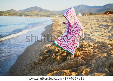 Happy little girl in beach towel having fun on the beach at Mediterranean sea in France. Cheerful kid enjoying vacation at the sea. Outdoor summer activities for children
