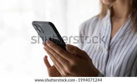 Close up unrecognizable young woman holding cellphone in hands, communicating distantly with friends, choosing goods in internet store, shopping online, web surfing information or playing game.