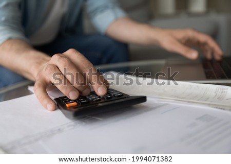 Close up young man managing household budget, calculating domestic expenditures, planning investments or managing savings earnings, paying bills or taxes, financial affairs, accounting concept. Royalty-Free Stock Photo #1994071382