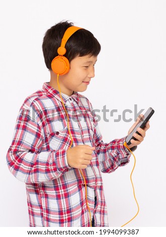 Happy Asian boy wears headphone and playing the cell phone on gray background, smile face