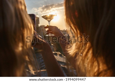 Girls take picture of a glass with wine over the setting sun on a party in a restaurant. Hospitality and catering service concept