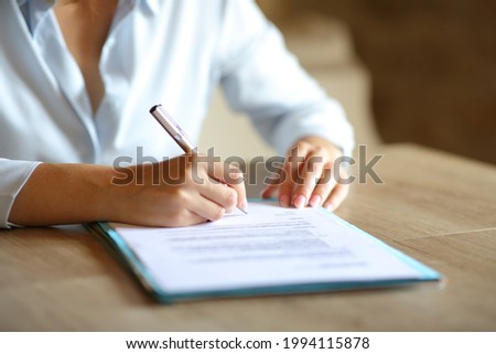 Close up of woman hands signing paper contract on table at home or office