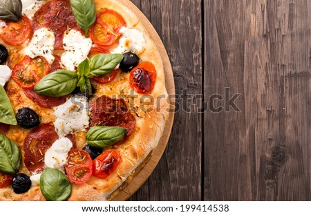 Rustic pizza with salami, mozzarella, olives and basil top view with copy space.