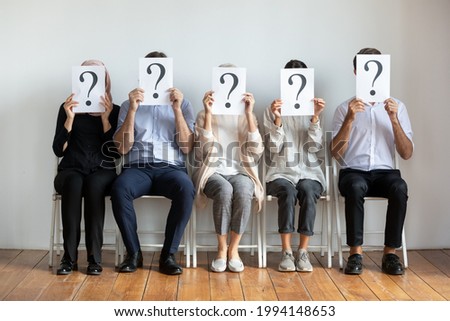 Diverse job candidates hiding faces behind sheets with question marks, sitting on chairs in row, business people waiting for job interview, human resources, employment and recruitment concept Royalty-Free Stock Photo #1994148653