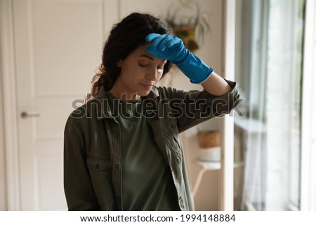 Tired stressed woman wearing rubber blue gloves cleaning, housekeeping and household concept, busy unhappy young female housewife feeling exhausted, touching forehead, doing chores at home Royalty-Free Stock Photo #1994148884