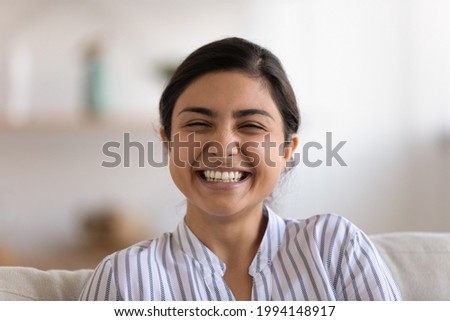 Close up profile picture of overjoyed millennial teen Indian female look at camera relaxing in cozy home. Headshot portrait of smiling young mixed race ethnicity woman have fun rest in living room.