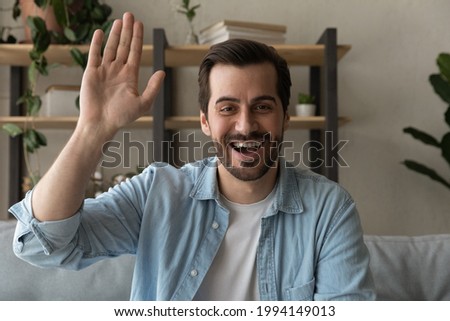 Joyful friendly young 30s man making hello gesture, starting remote video call meeting with friends. Happy smiling handsome male blogger streaming in social network, distant communication concept. Royalty-Free Stock Photo #1994149013