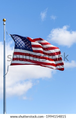 American flag flying in a breeze against a sunny blue sky with light white clouds
