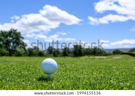 White golf ball sitting on a white tee in the tee box, hole long way in the distance
