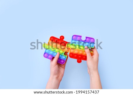 Popit toys in the form of puzzles in hands on a blue background. Multicolored Pop it toy