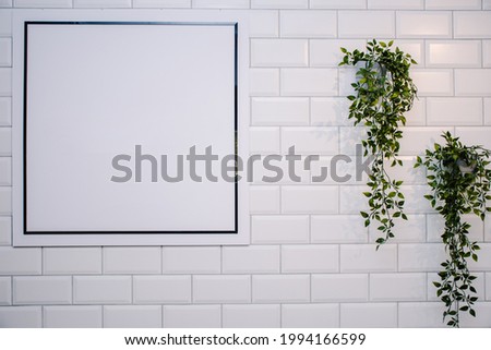 Blank sign on a white brick wall with some plants. Ideal for logo mock up
