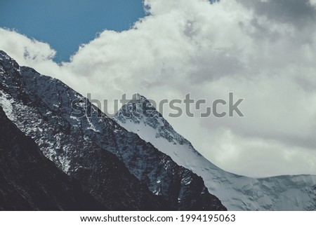 Atmospheric mountain landscape with high snowy peaked top under cloudy sky in faded tones. Gloomy mountain scenery with great snow-covered pinnacle in clouds in dark colors. Awesome snowy pointy peak.