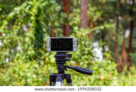 A mobile phone mounted on a tripod capturing image of natural forest in Wonogiri, Indonesia. Selected focus.