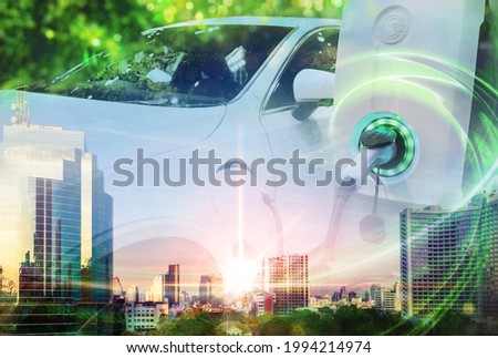EV Car or Electric vehicle concept with double exposure on cityscape background, Power cable supply plugged in on blurred nature with green energy power effect. Eco-friendly sustainable energy. Royalty-Free Stock Photo #1994214974