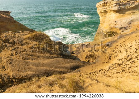In the photo we see the ocean and the sand spit, the rocky sandy shore. The water in the ocean is emerald. Light white waves. There is no one in the photo. High angle view.