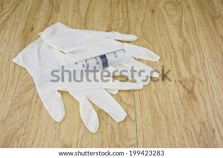 Big plastic syringe place on latex gloves with wood background. Healthcare and medical concepts photography.