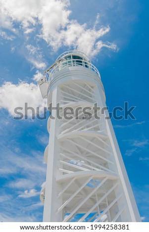 Low angle view of white lighthouse against blue sky with puffy white clouds.