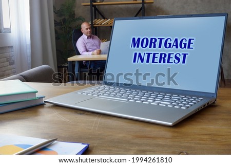 Financial concept about MORTGAGE INTEREST with sign on the Compact laptop A successful Banker with documents on the background 
