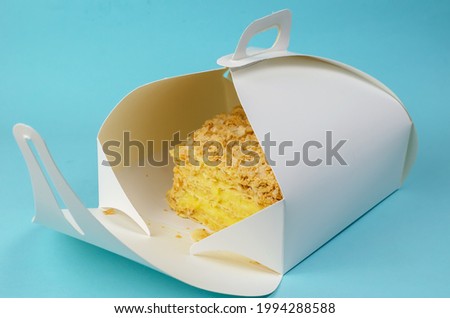 The cake is packaged in a white paper box on a light blue background. Open Kraft packaging with a piece of sweet layer cake. Eco-friendly Lunch Box. Food to take away concept.