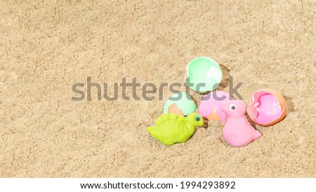 Green and pink dinosaurs made from plasticine beside egg shells. Sand background. Kid's toy. Minimal concept.