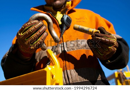 Safety workplace close up image of trained competent rigger high risk worker wearing safety heavy duty glove inspecting D- shape shackle pin prior inserting into crane lifting lug cate during lifting  Royalty-Free Stock Photo #1994296724