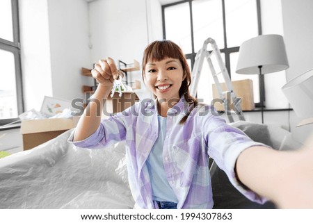 moving, people and real estate concept - happy smiling asian woman with house keys taking selfie or having video call at new home