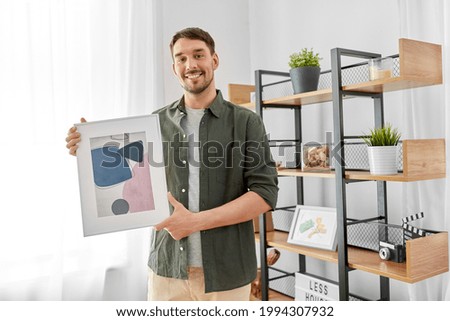 home improvement, decoration and people concept - happy smiling man decorating room with abstract picture in frame