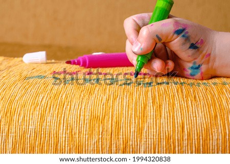Dirty children's hand in colored markers draws with a green felt-tip pen of the couch. daily life dirty stain for wash and clean concept. High quality photo Royalty-Free Stock Photo #1994320838