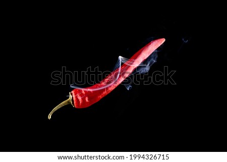 Chilli peppers isolated. Spicy chile cayenne pepper with abstract fog or steam mist cloud. Red hot chili paprika with tongue of fire flame on black background. Fresh spice vegetable concept