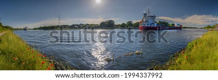 Panoramic view of Kiel Kanal in summer with cargo ships, swans and blooming poppies.