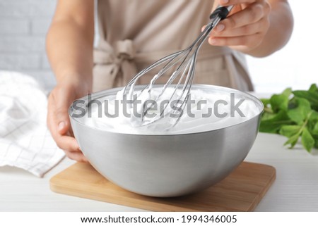 Woman whipping white cream with balloon whisk at wooden table, closeup Royalty-Free Stock Photo #1994346005