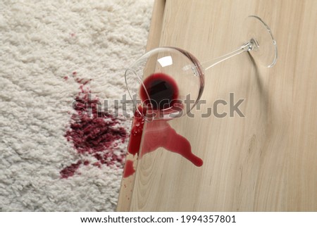 Overturned glass and spilled red wine on white carpet indoors, above view Royalty-Free Stock Photo #1994357801