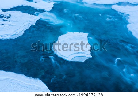 Long exposure shot of blue water stream flowing around ice. Unfrozen Katun river in winter Royalty-Free Stock Photo #1994372138