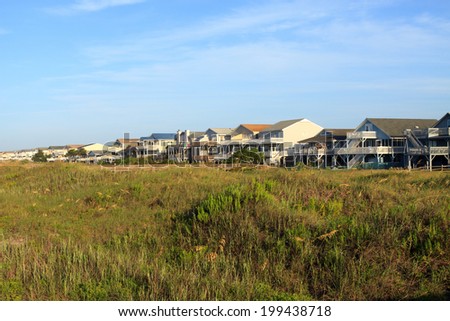 Color DSLR landscape picture of luxury beach vacation houses across the green sand dunes, in Sunset Beach, North Carolina.  The image is in horizontal orientation with ample copy space for text.