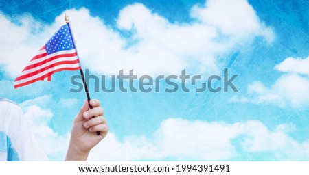 Composition of caucasian hand holding american flag over blue sky with clouds. american patriotism, independence and celebration concept digitally generated image.