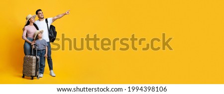 Family Travel Concept. Happy middle eastern parents with little daughter carrying suitcases and pointing aside at copy space on yellow background, mom, dad and child ready for vacation, panorama Royalty-Free Stock Photo #1994398106